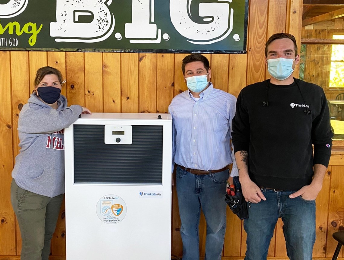 Here Matt Gallant Vice President of Operations with ThinkLite and Jen Forester, Director of Camp Wonderland adjust the settings on a newly installed Flair Air Quality Monitor. The monitor will measure for harmful pathogens and volatile organic compounds along with CO2, humidity, and temperature levels.