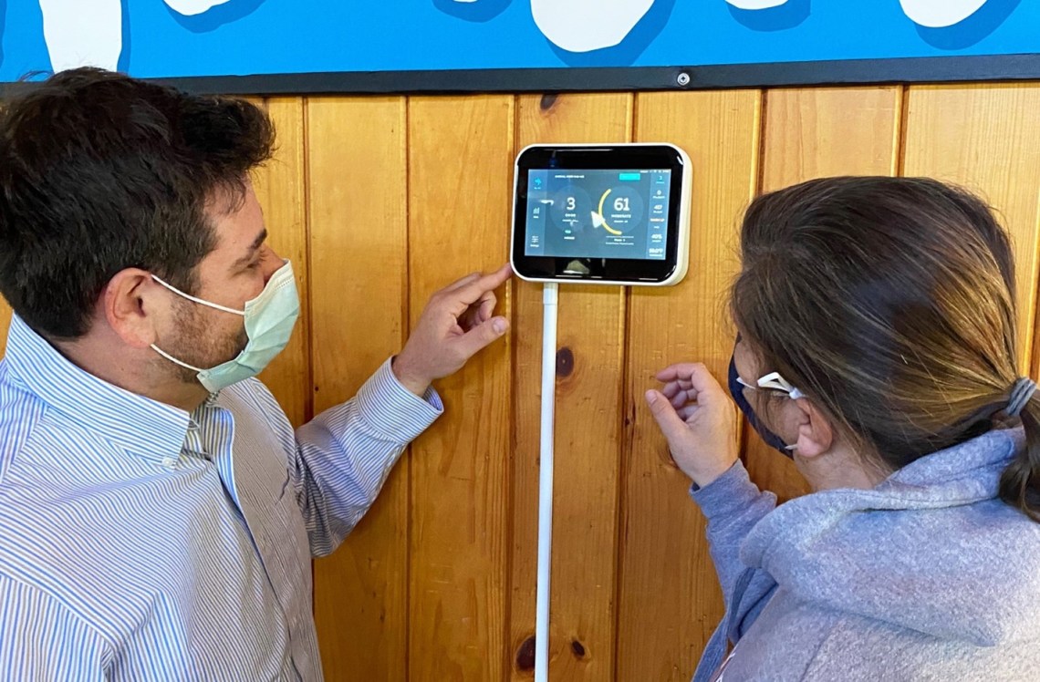 Here Matt Gallant Vice President of Operations with ThinkLite and Jen Forester, Director of Camp Wonderland adjust the settings on a newly installed Flair Air Quality Monitor. The monitor will measure for harmful pathogens and volatile organic compounds along with CO2, humidity, and temperature levels.